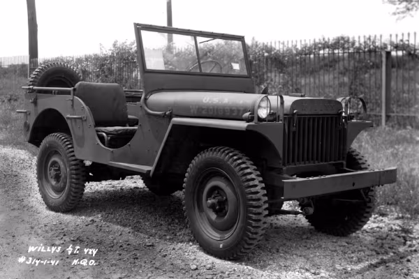 Veículo com traços retos, pneus robustos, sem capota e uma grade vertical na parte dianteira.